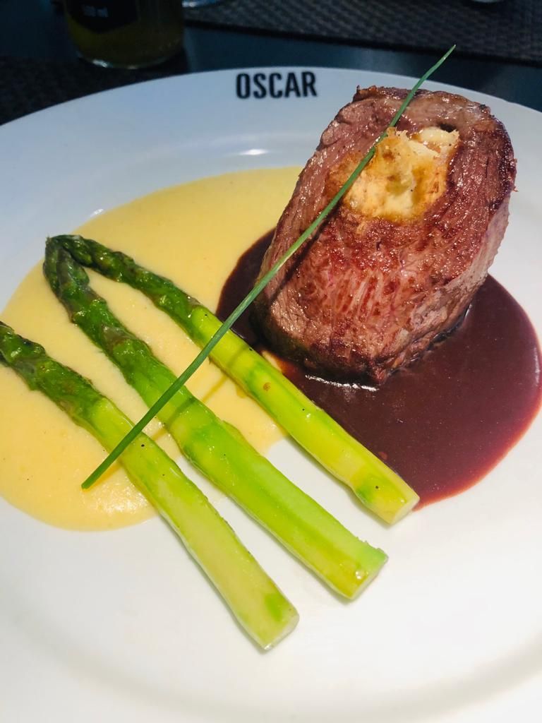 Bife Oscar com aspargos e molho em um prato branco, jantar requintado.