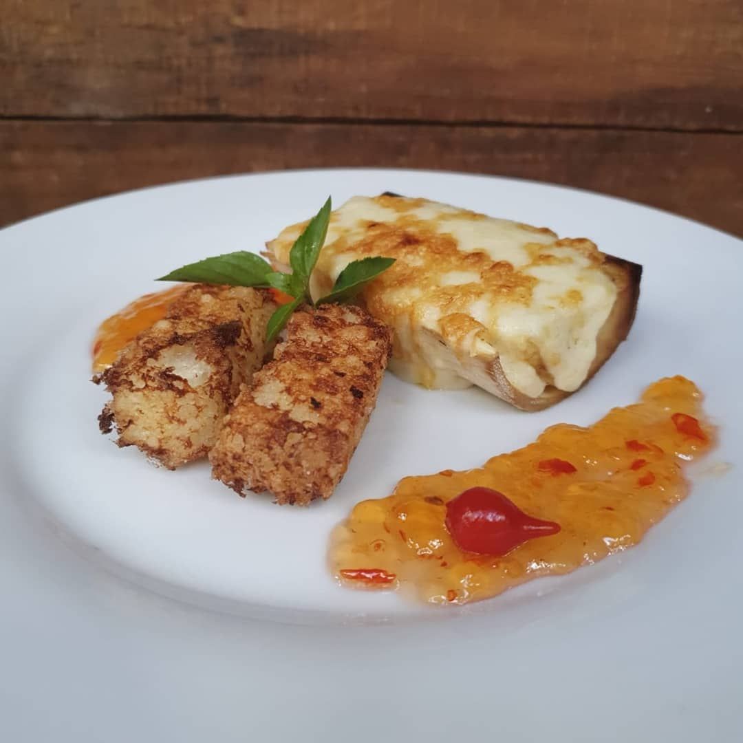 Prato com pão com queijo, pedaços de batata frita e molho de pimenta doce.