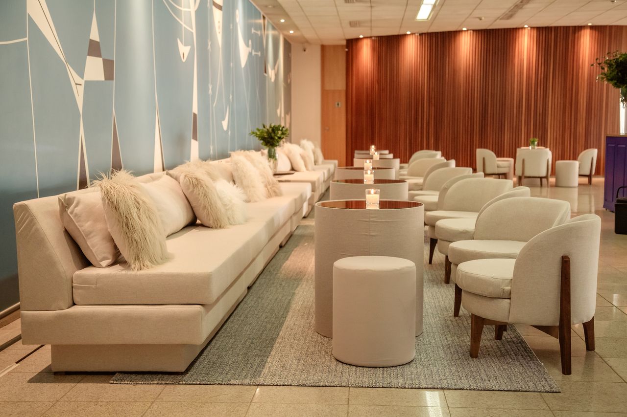 Sala de estar com sofás e cadeiras em tom creme, mesas com tampos de cobre e parede azul claro com decorações.