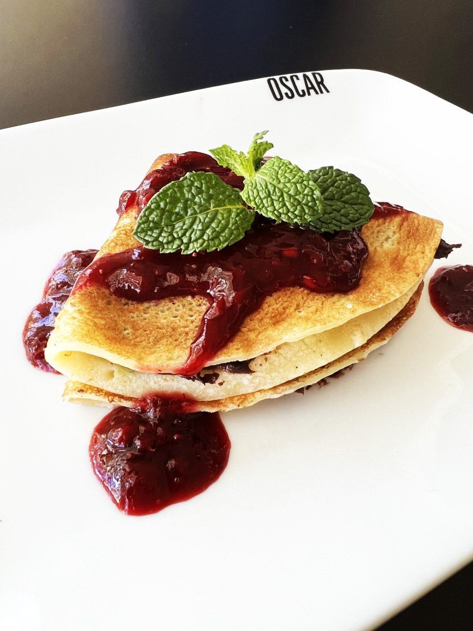 Crepe com molho de frutas vermelhas e guarnição de hortelã em um prato branco.