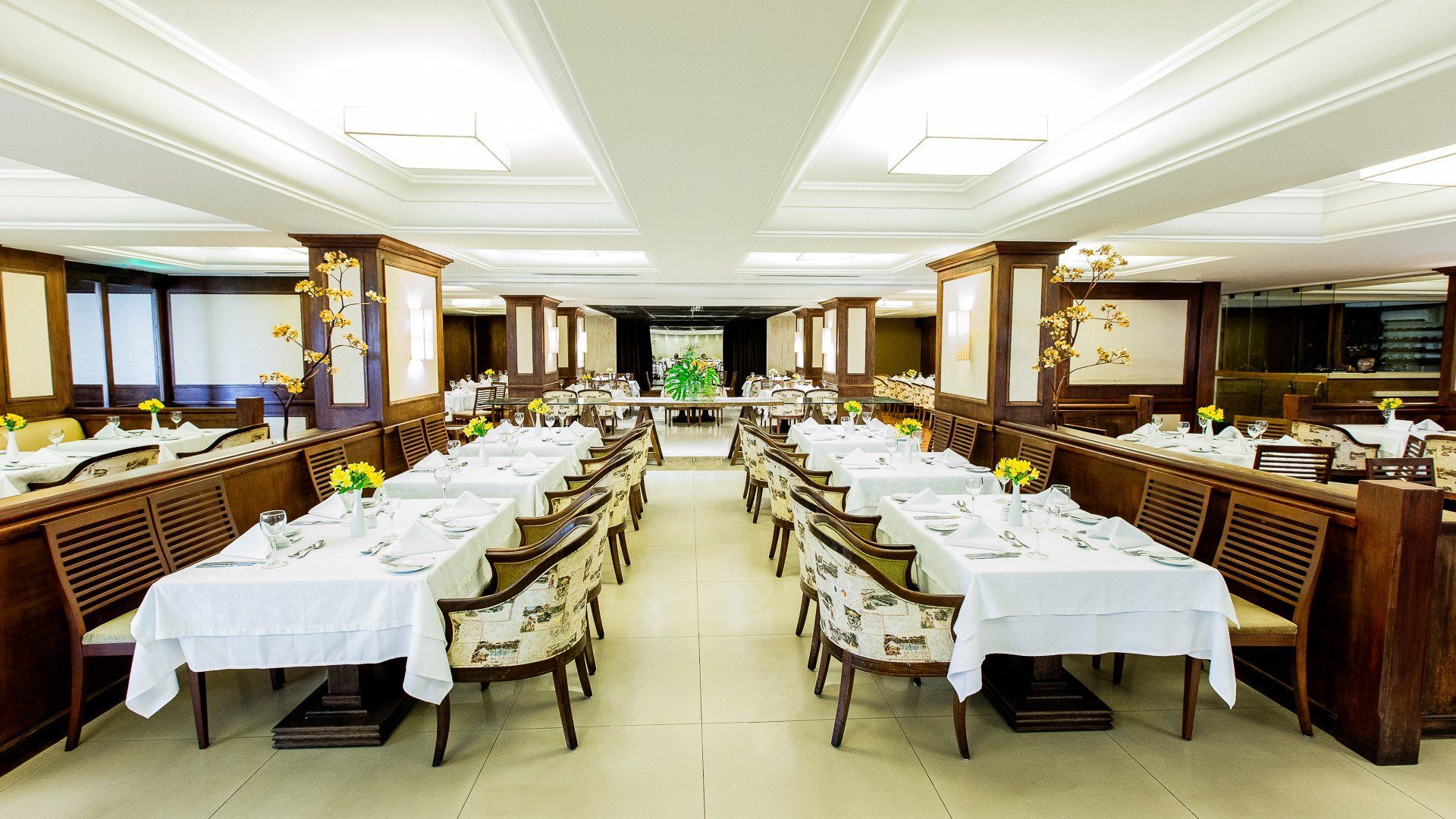 Sala de jantar formal de restaurante com longas fileiras de mesas preparadas para os hóspedes.