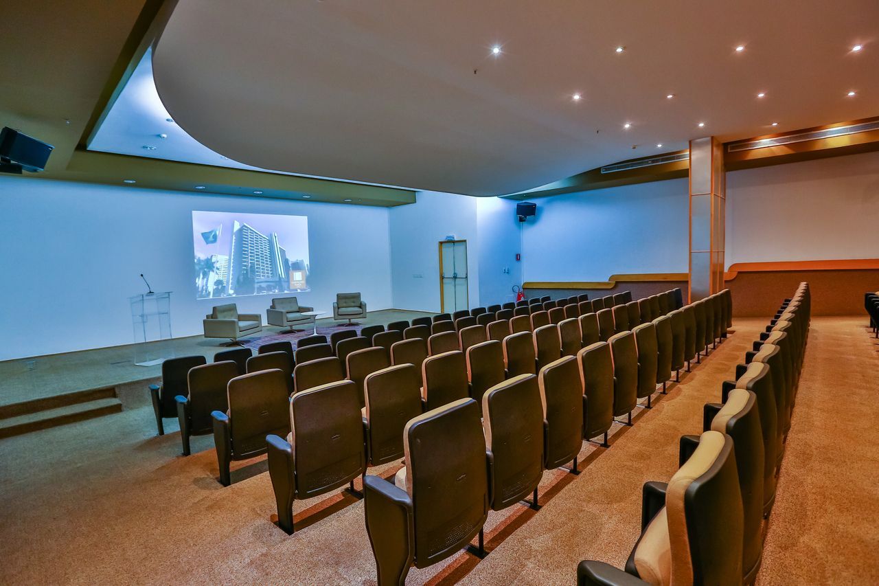 Quarto de hotel aconchegante com cama king-size, bancos, luminárias e uma estante iluminada decorativa.