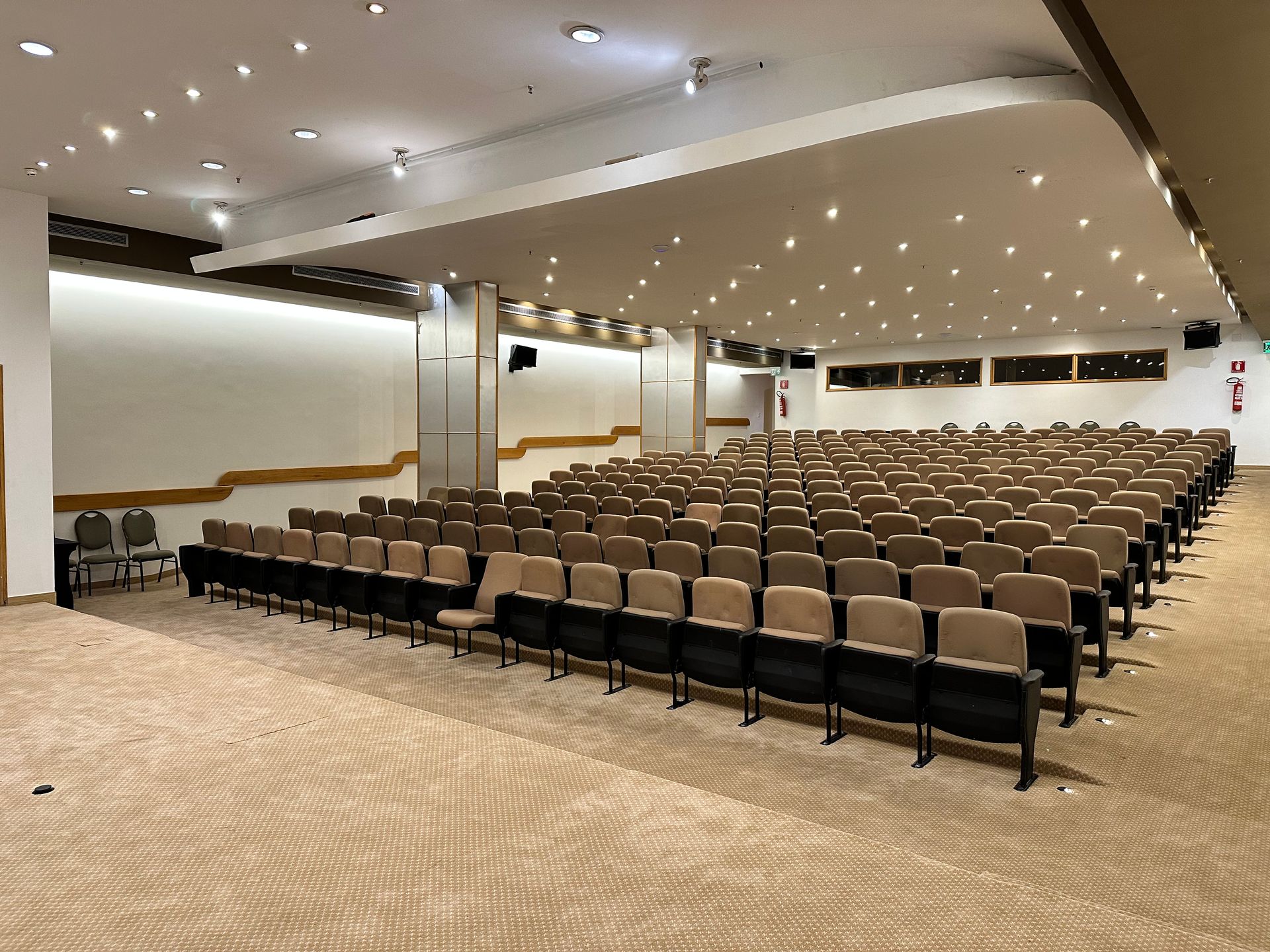 Auditório com fileiras de assentos de frente para uma tela exibindo uma apresentação. Iluminação aconchegante.