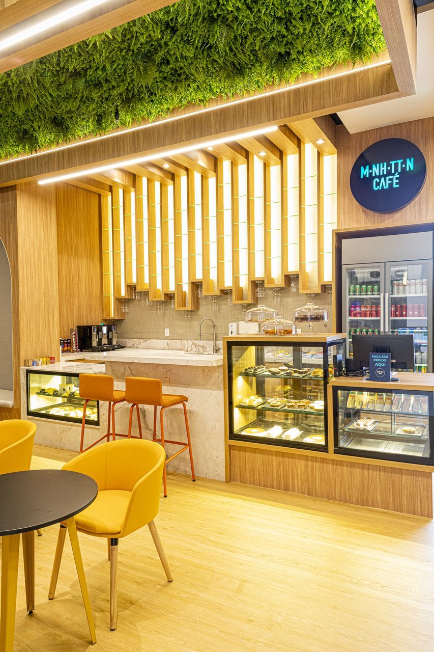 Interior de cafeteria com cadeiras amarelas, um balcão, vitrines e uma placa.