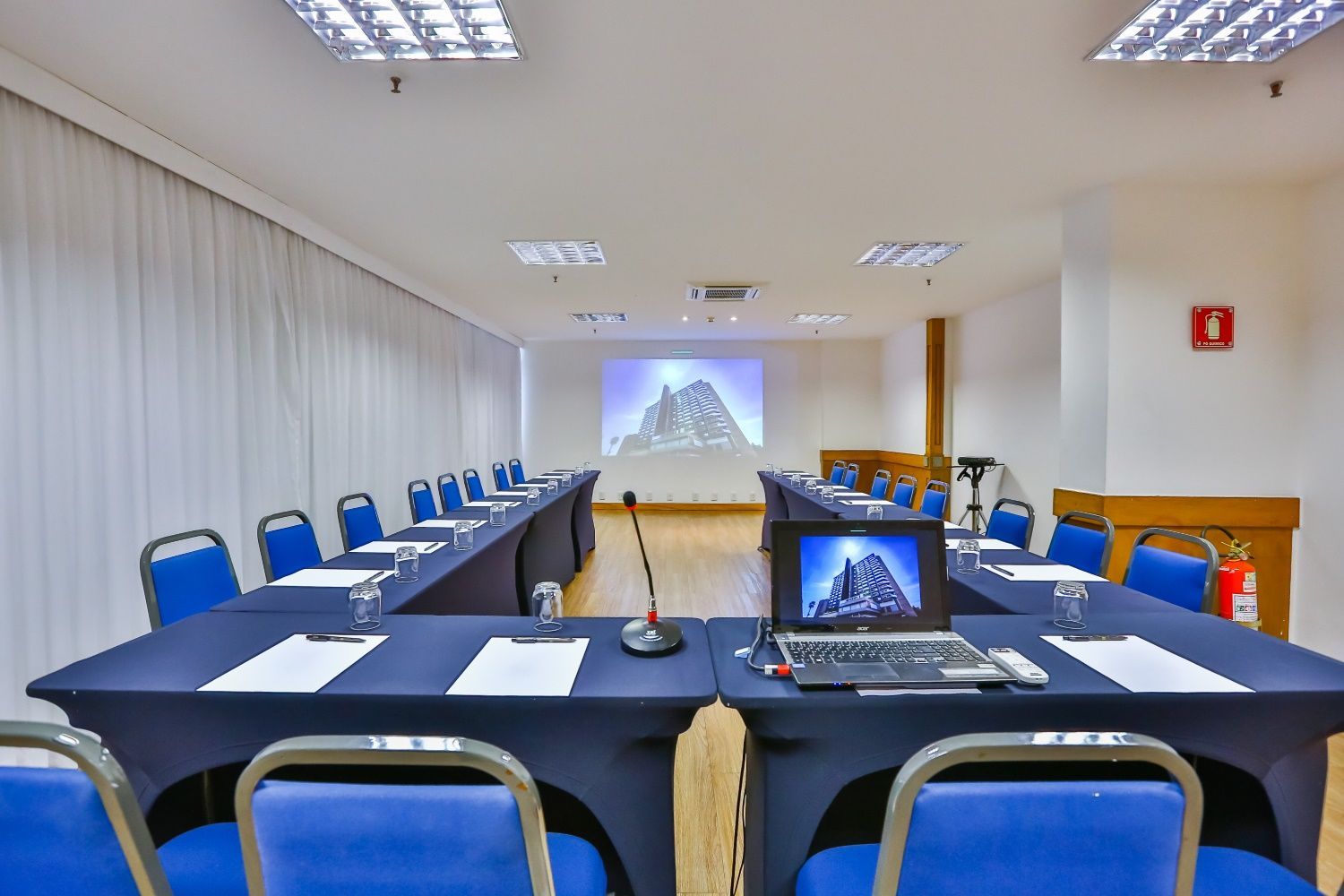 Sala de conferências com uma mesa em formato de U, laptop e tela de projetor exibindo uma montanha.
