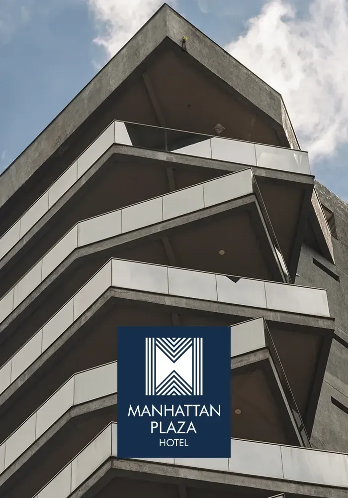 Exterior do Manhattan Plaza Hotel com varandas angulares e escalonadas; logotipo azul na parte inferior.