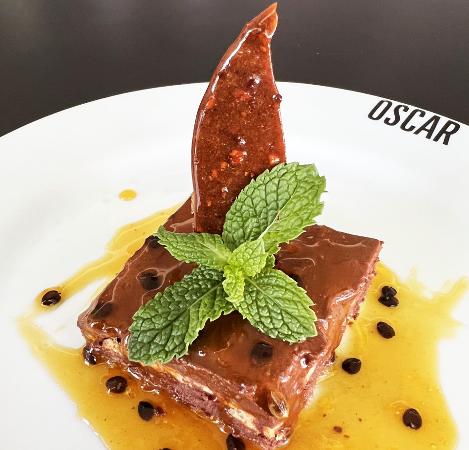 Sobremesa de chocolate em um prato branco com guarnição de hortelã, calda e decoração de chocolate.