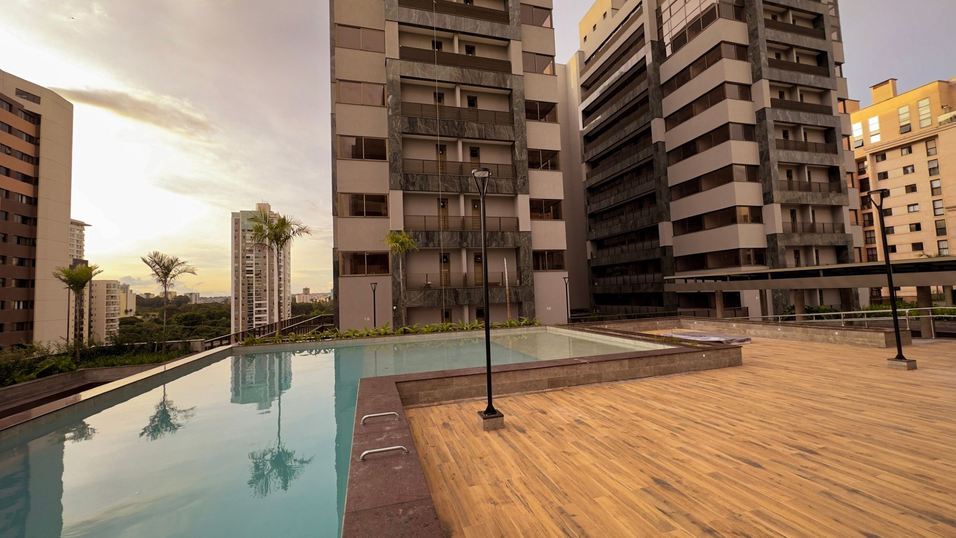 Uma piscina infinita em um terraço de um arranha-céu ao pôr do sol, cercada por prédios de apartamentos modernos e palmeiras.