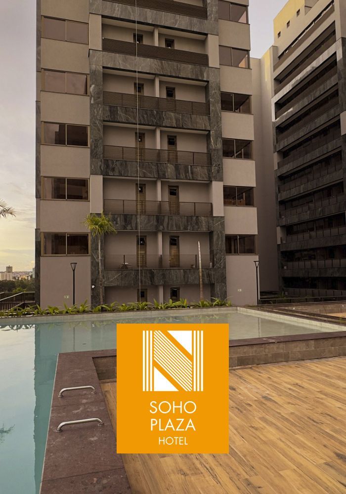 Exterior do Manhattan Plaza Hotel com varandas angulares e escalonadas; logotipo azul na parte inferior.