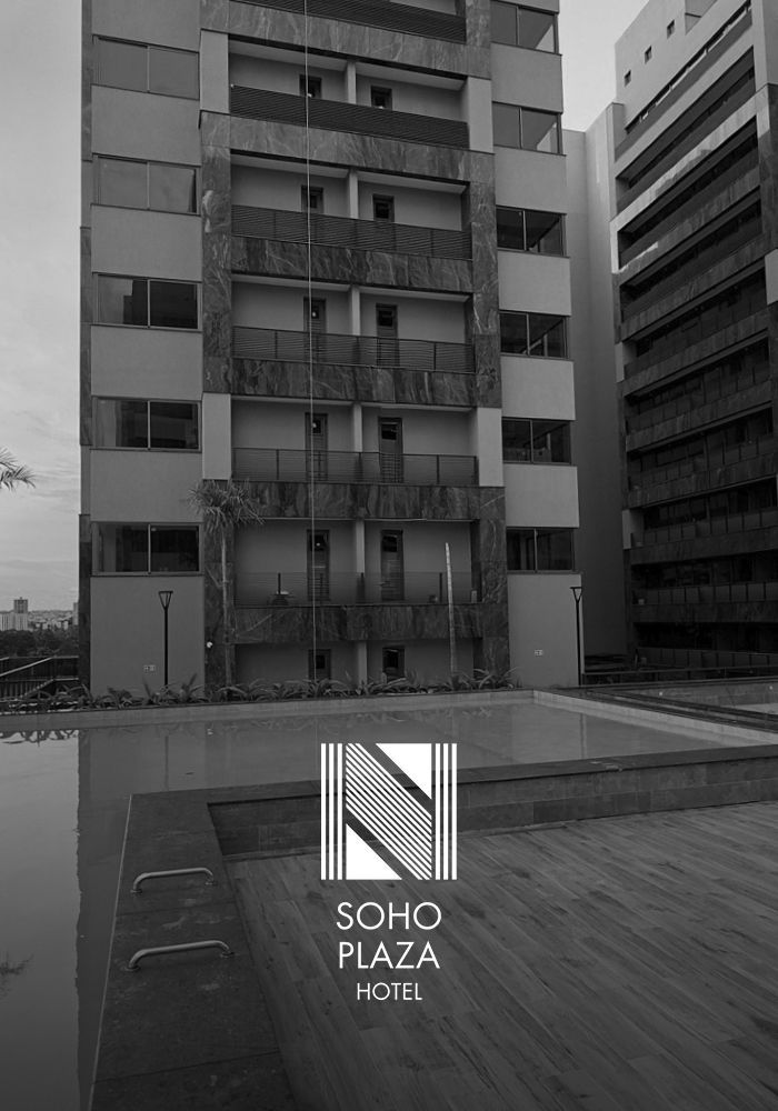 Vista em preto e branco de um edifício de hotel de vários andares com varandas com vista para uma piscina, apresentando o logotipo do Soho Plaza.
