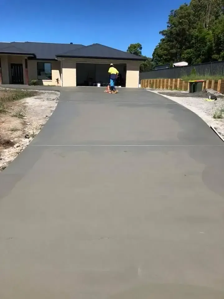 A Man Is Walking Down A Concrete Driveway In Front Of A House — Luke Seears Concreting in Port Macquarie, NSW