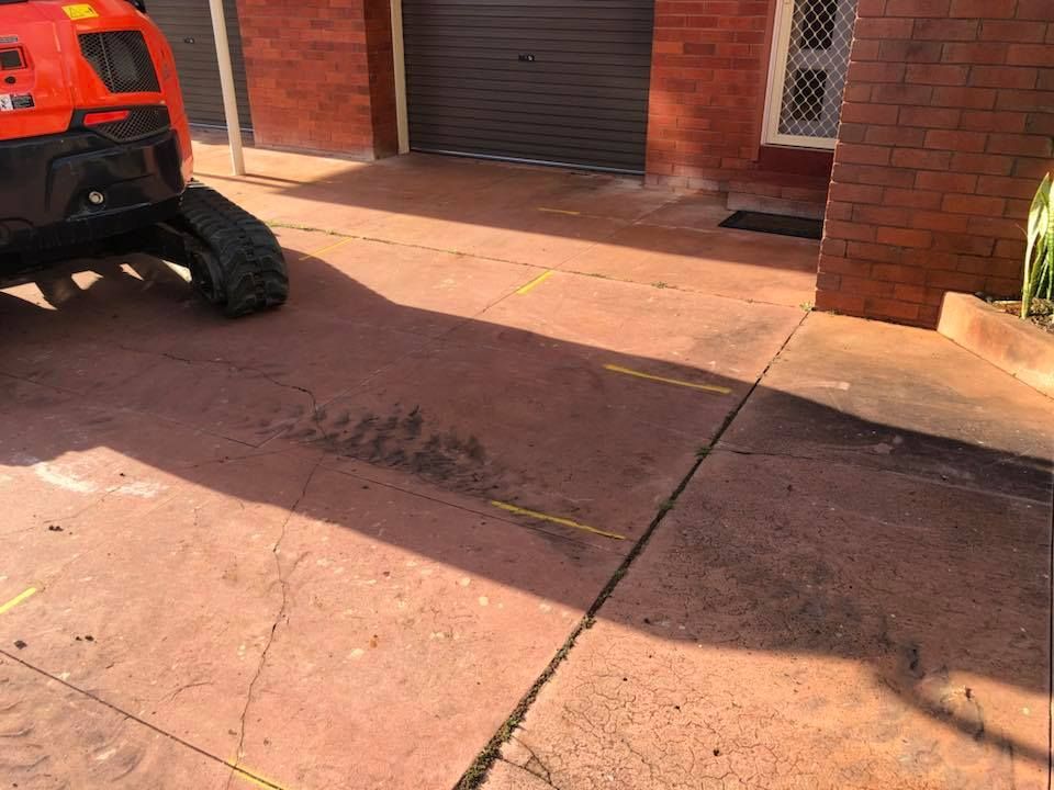 An Orange Tractor Is Parked In A Driveway Next To A Brick Building — Luke Seears Concreting in Laurieton, NSW
