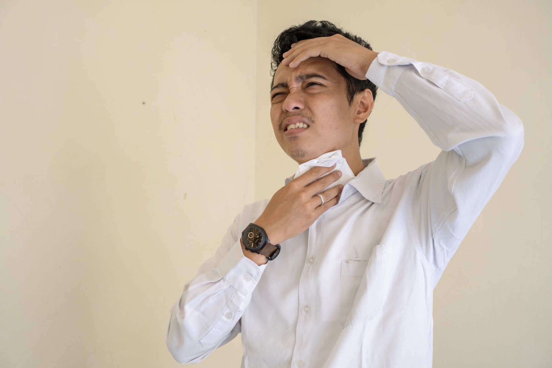A man in a white shirt is wiping his forehead with a napkin.