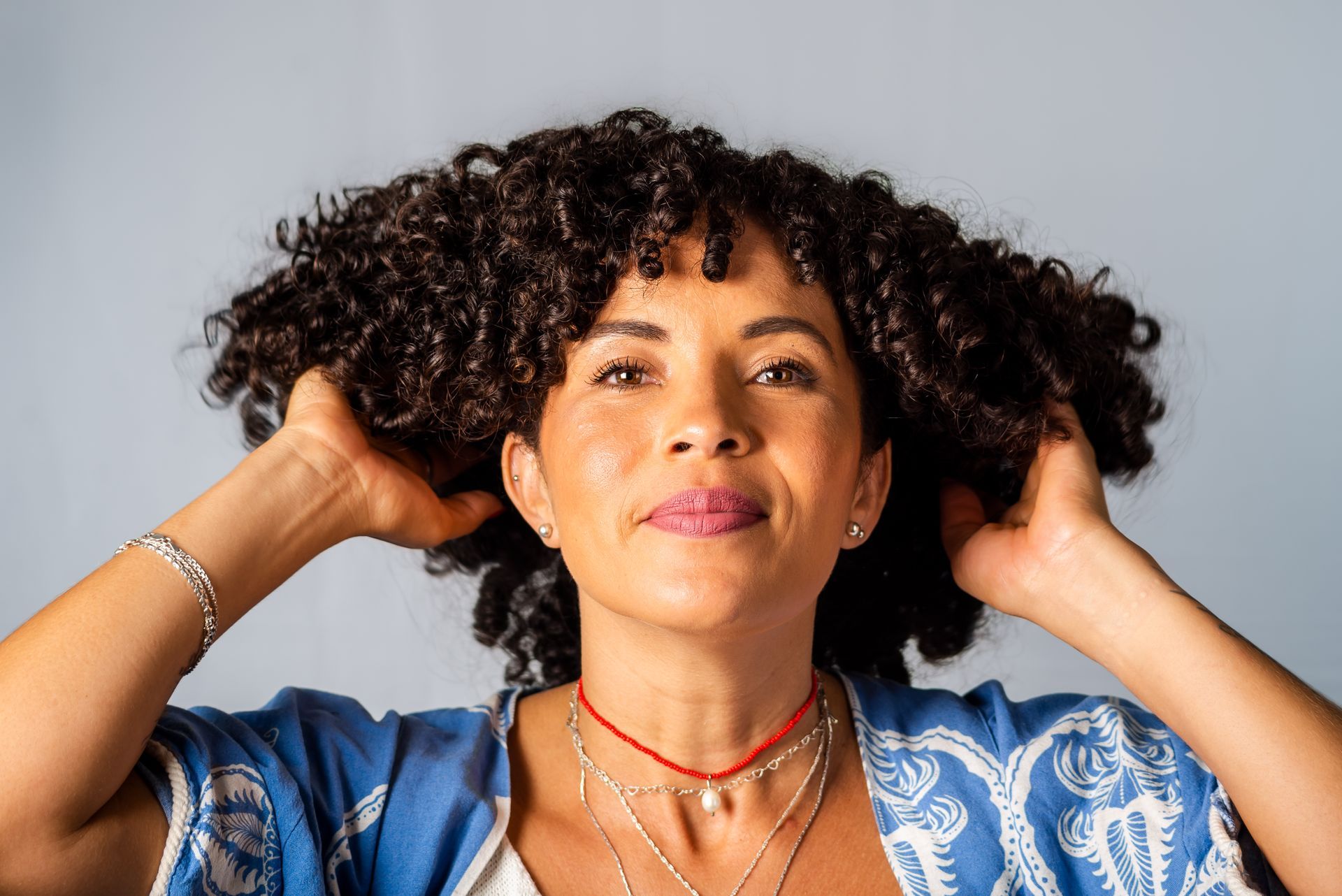 A woman with curly hair is holding her hair in her hands.