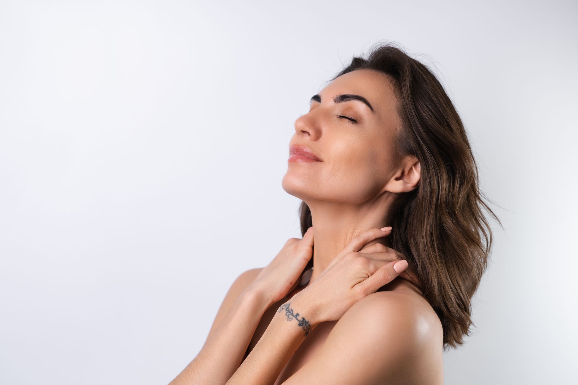 Woman with eyes closed, hands on neck, illuminated against a white background.
