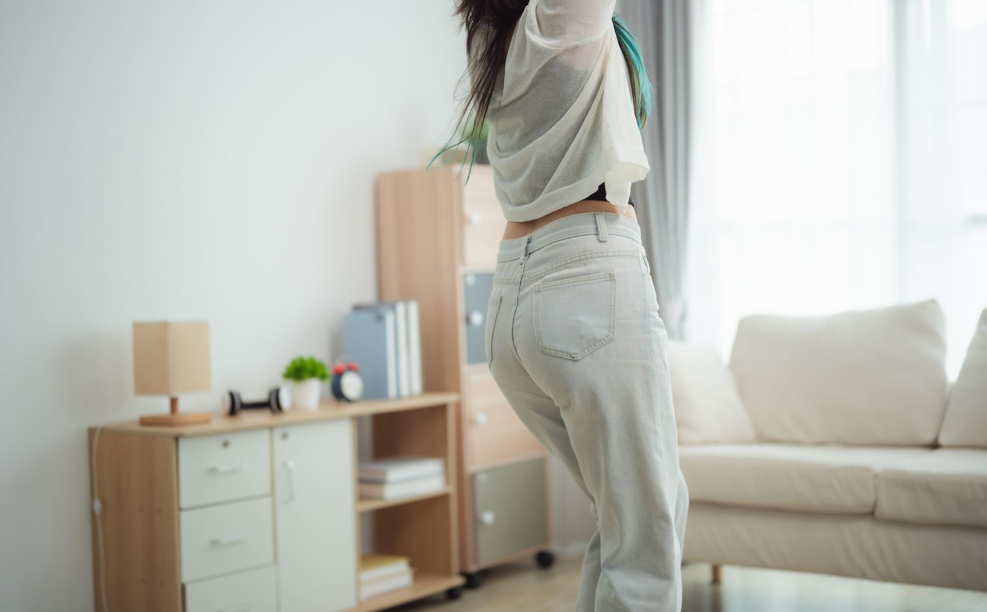 A woman is dancing in a living room in front of a couch.