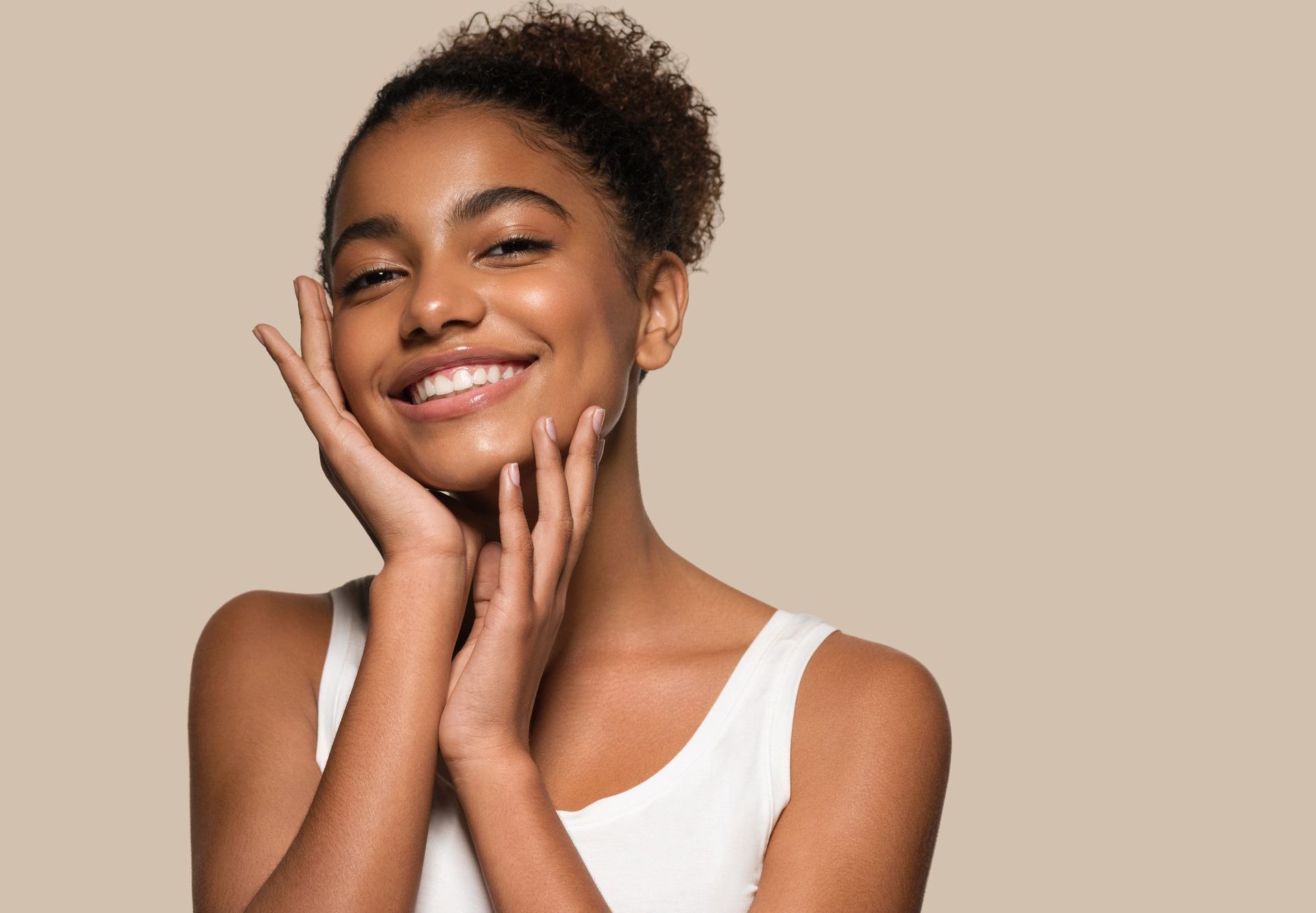 A woman is smiling and touching her face with her hands.