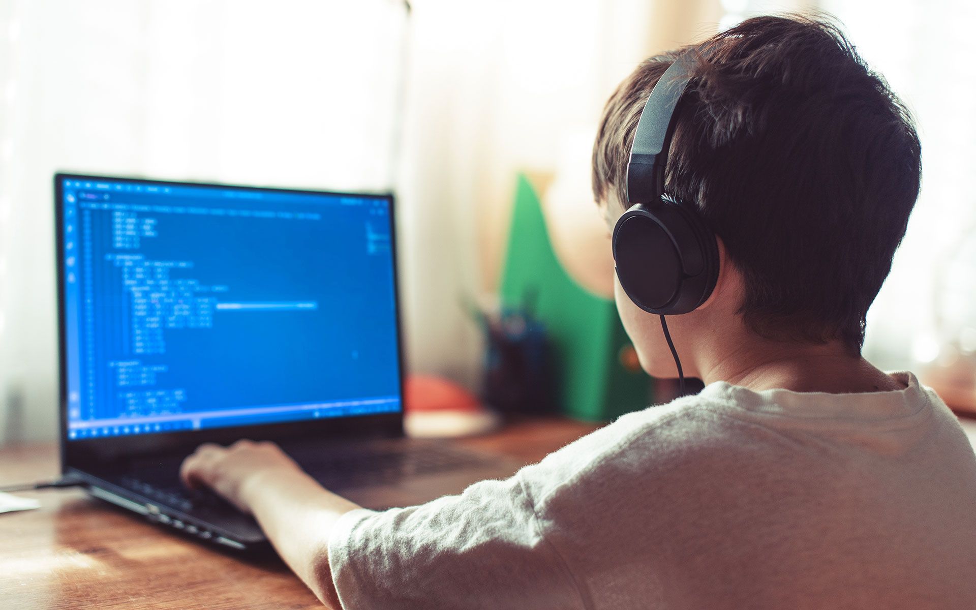 A person wearing headphones works on a laptop, viewing code on the screen.