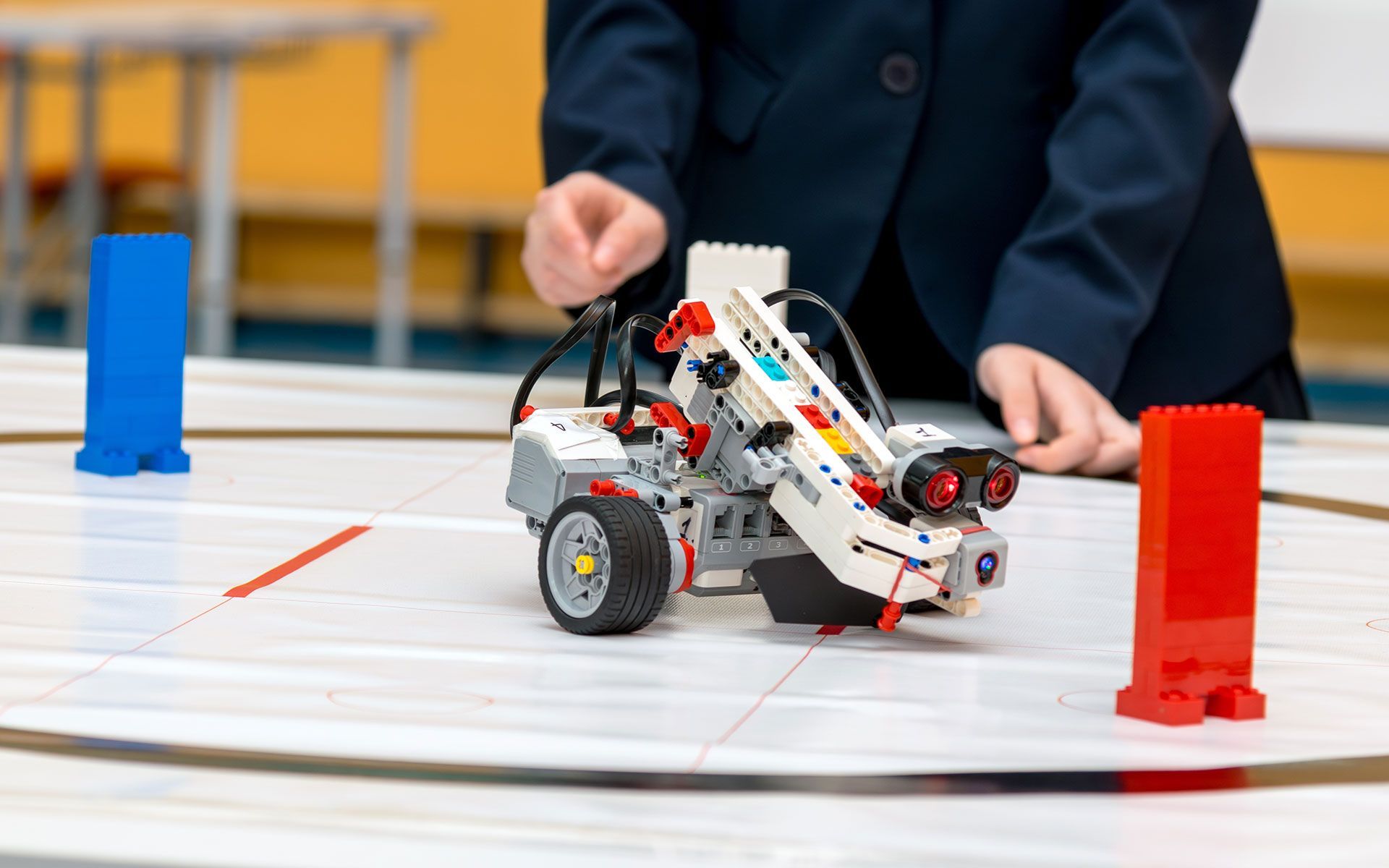 A person operating a LEGO robot on a white surface with blue and red blocks.