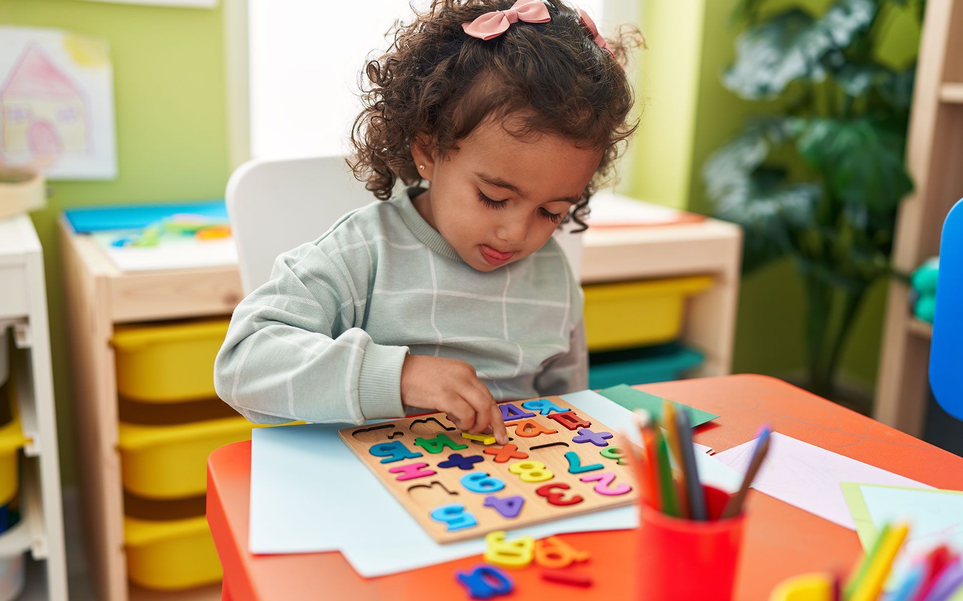 Young child placing a number piece into a wooden puzzle at a table.