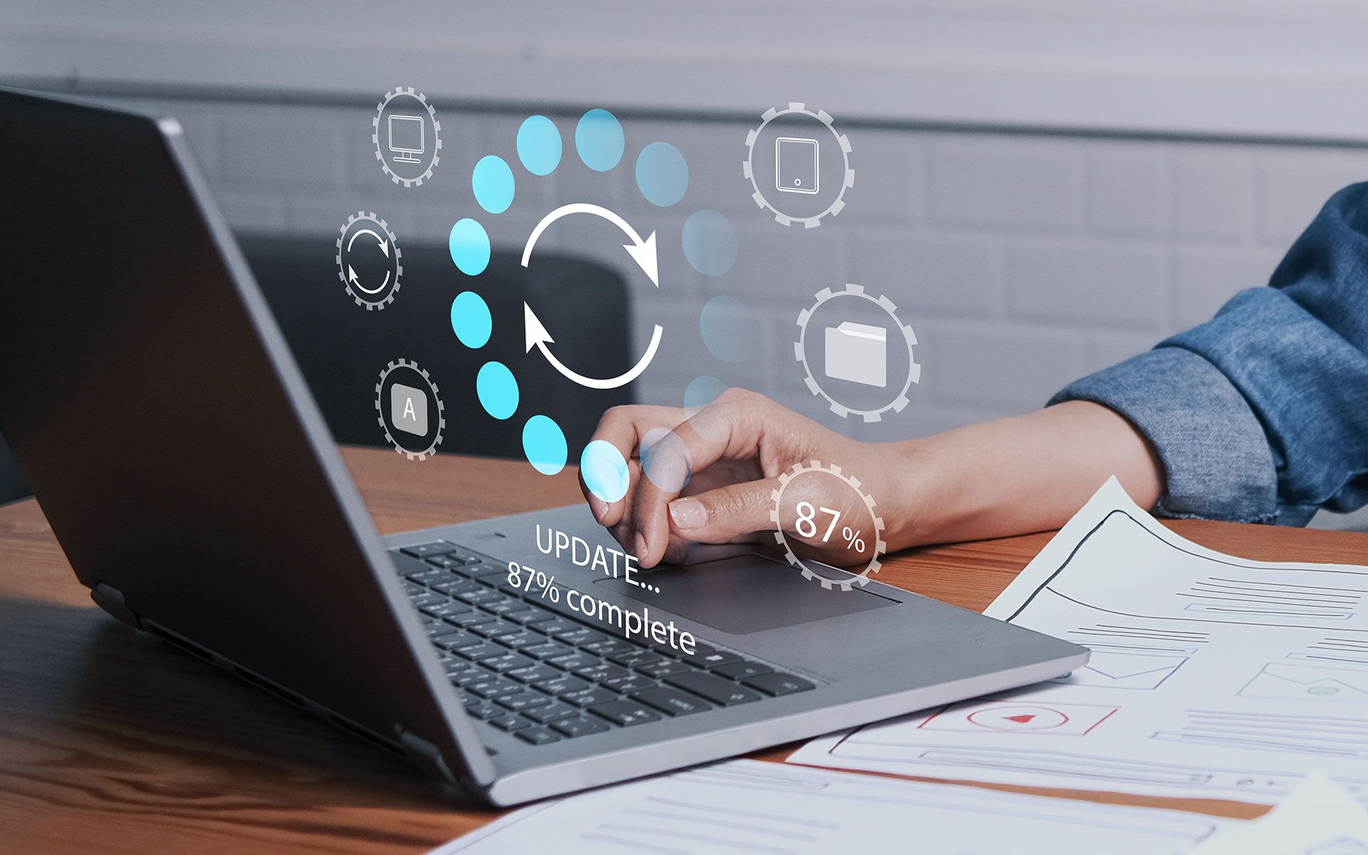 Person updating laptop software with digital icons floating above.