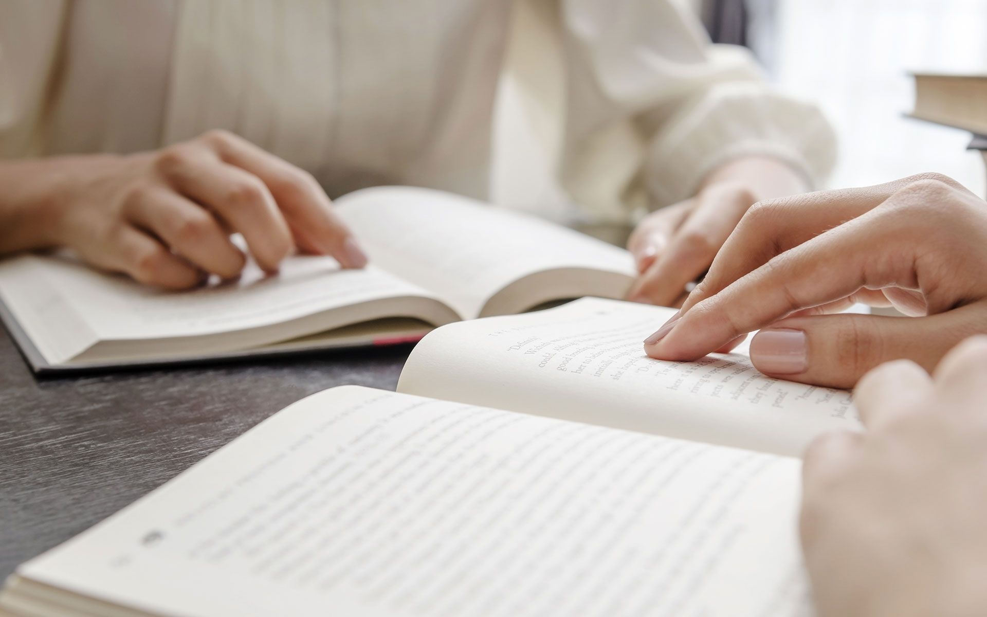 Hands pointing at open books on a table, possibly studying or reading together.