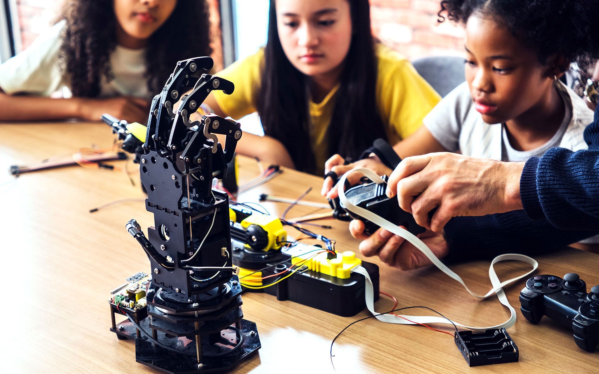 Three children watch an adult operate a robotic hand.