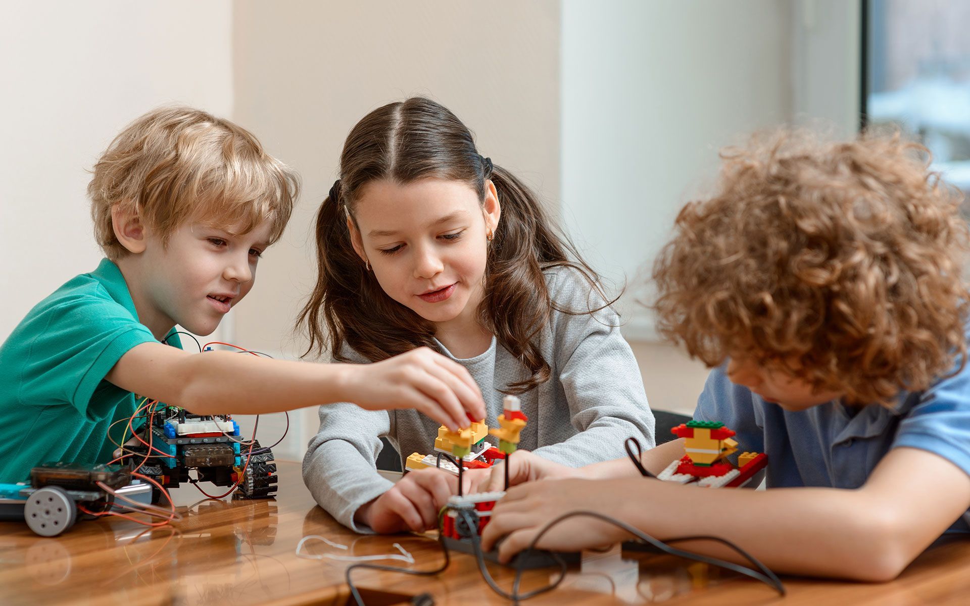 Three children building with colorful blocks and wires at a table.