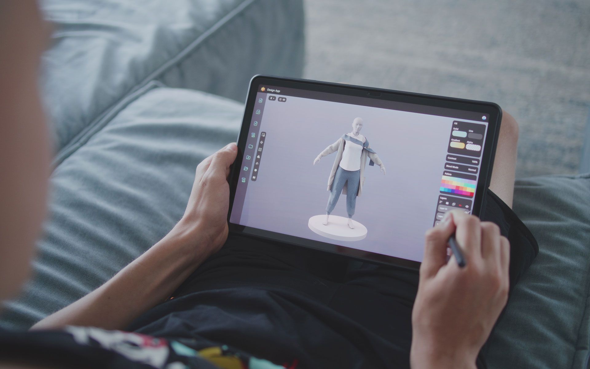 Person using a tablet to design a 3D model, sitting on a couch.