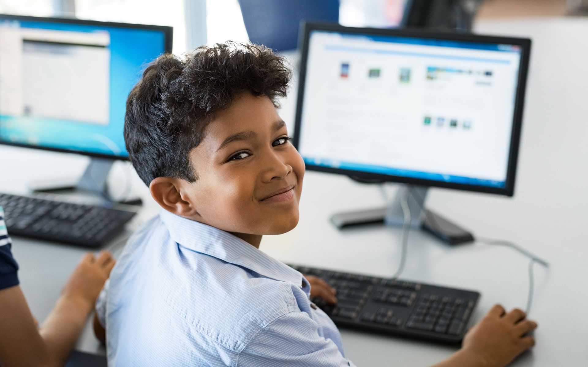 Boy smiling at the camera while working on a computer in a computer lab.