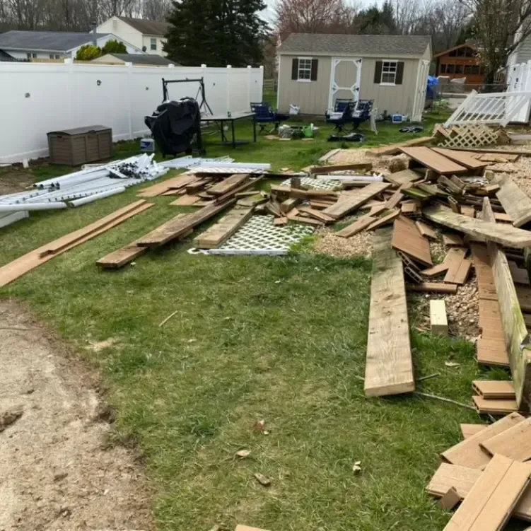 A pile of wood in a yard with a white fence in the background