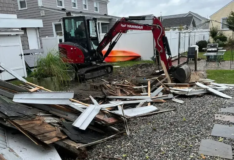 A red excavator is sitting on top of a pile of wood in front of a house.