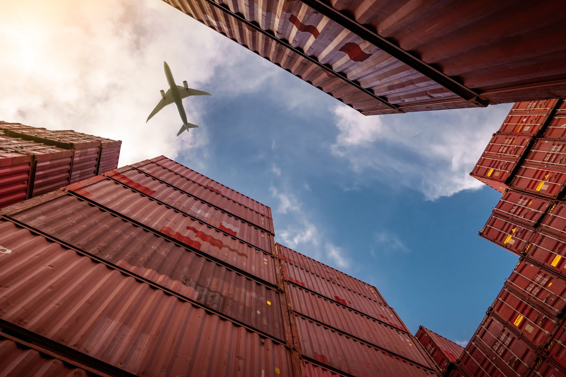 Shipping containers stacked, framing a sky with an airplane.