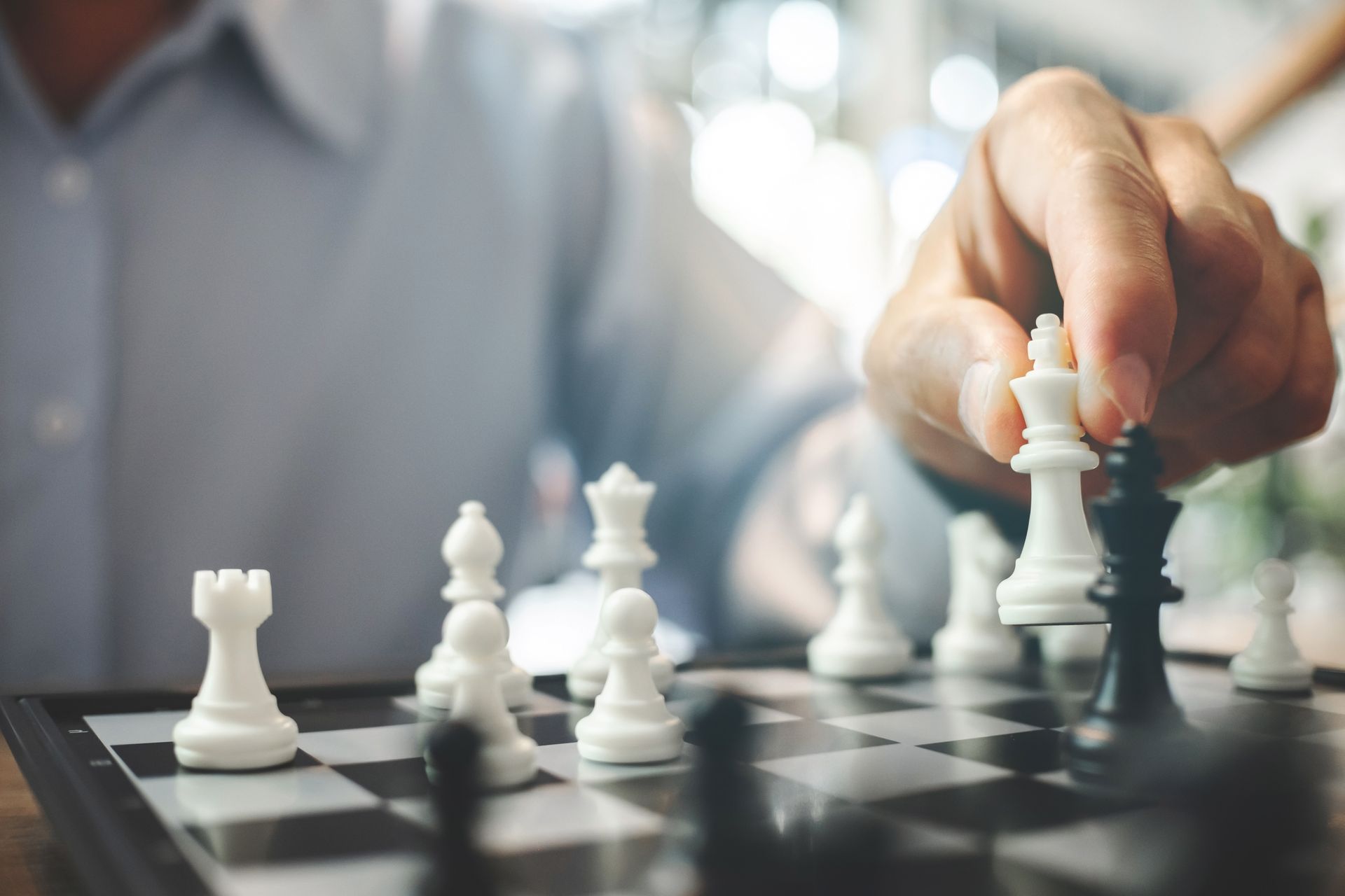 Person moving a white king chess piece, nearing the black king, on a chessboard.