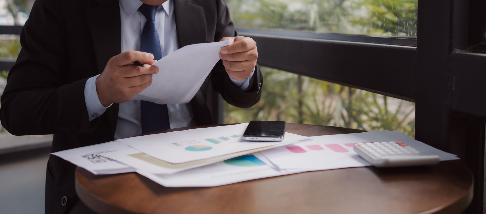 A man in a suit reviews paperwork at a table with a calculator and charts.