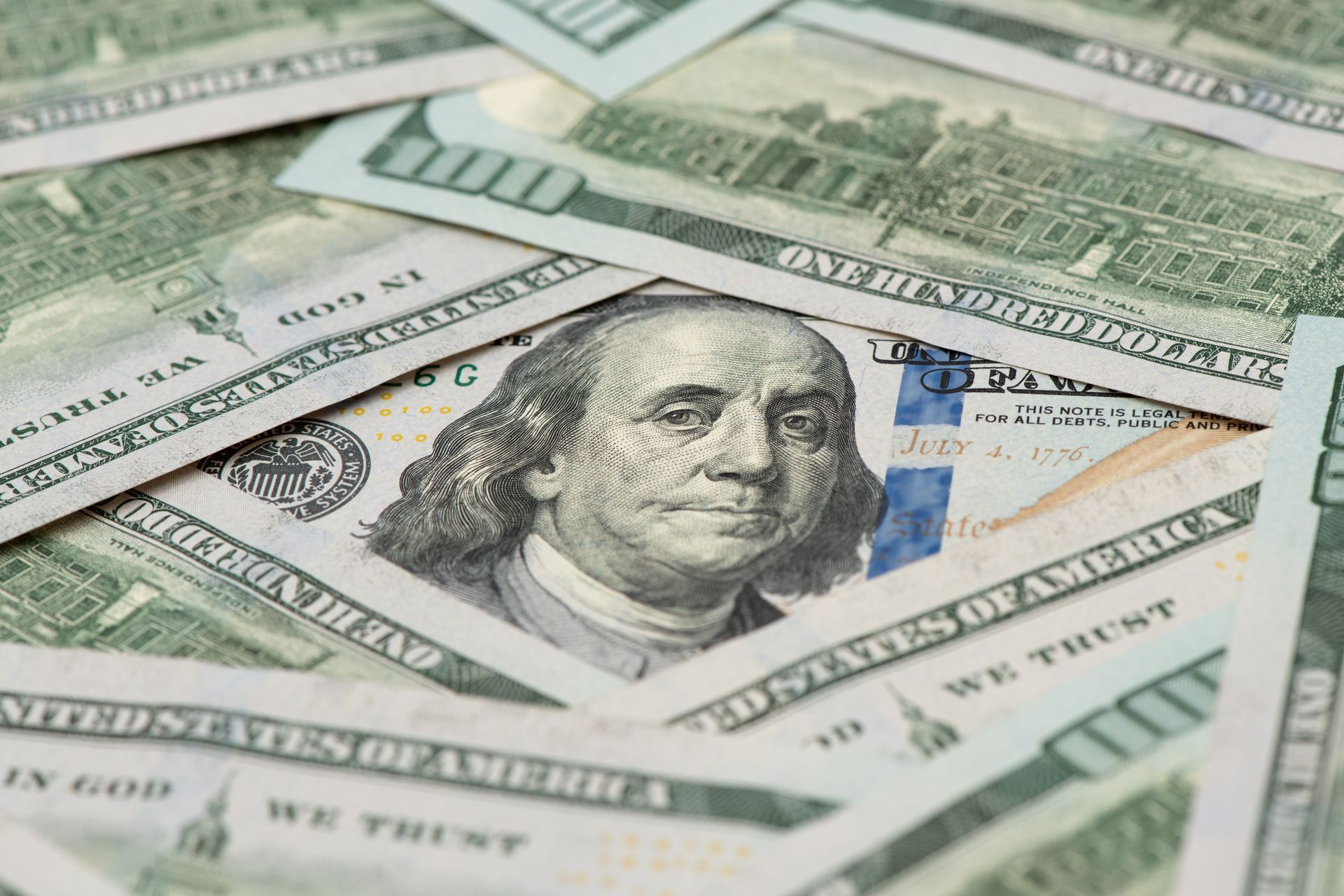Pile of US $100 bills, with Benjamin Franklin's face visible, angled close up.