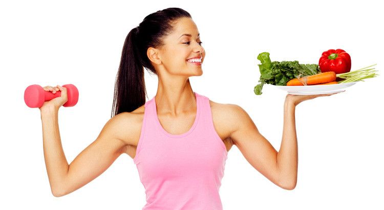 woman holding up a barbell and vegetables