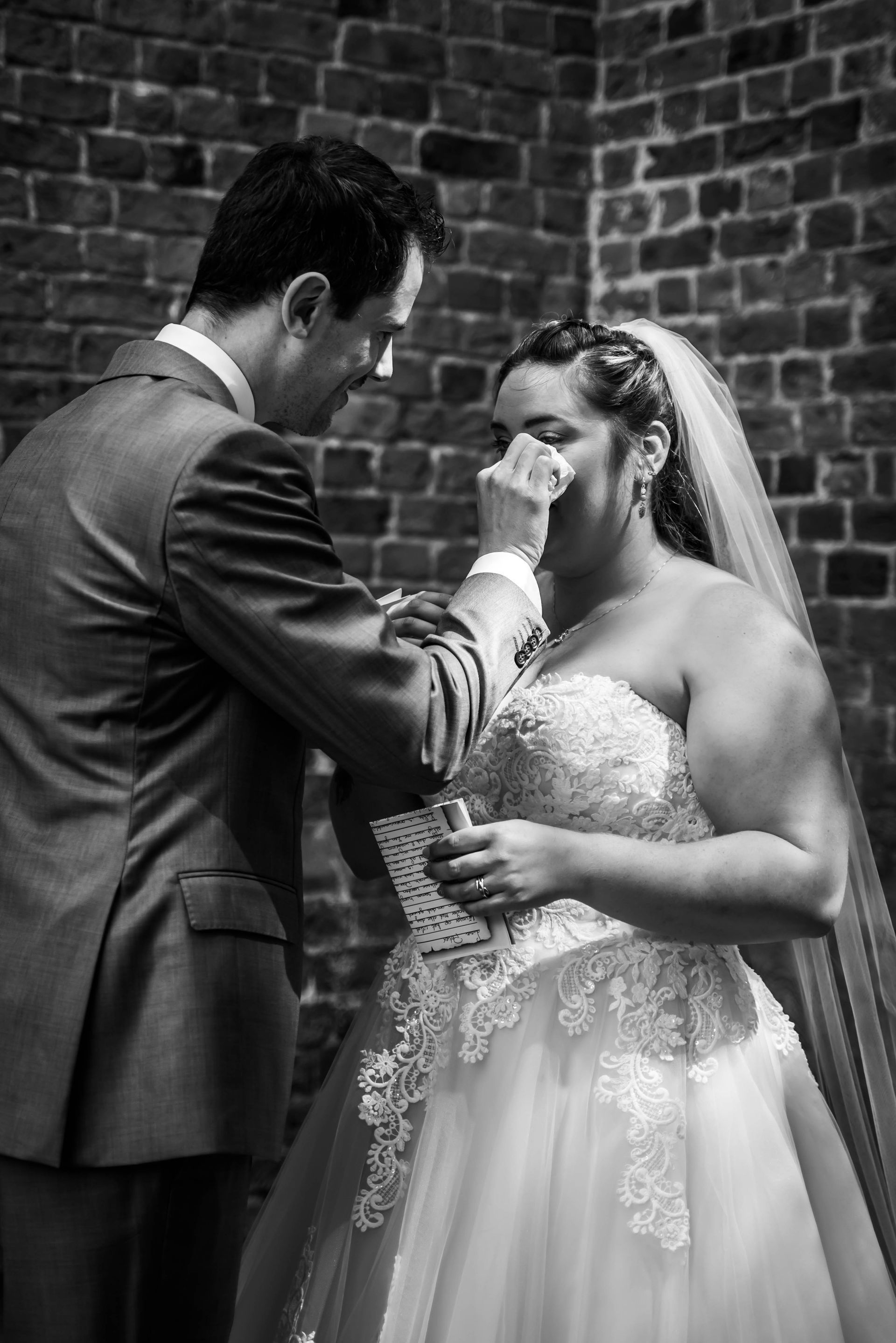 Een bruid en bruidegom staan ​​voor een bakstenen muur en de bruid huilt.
