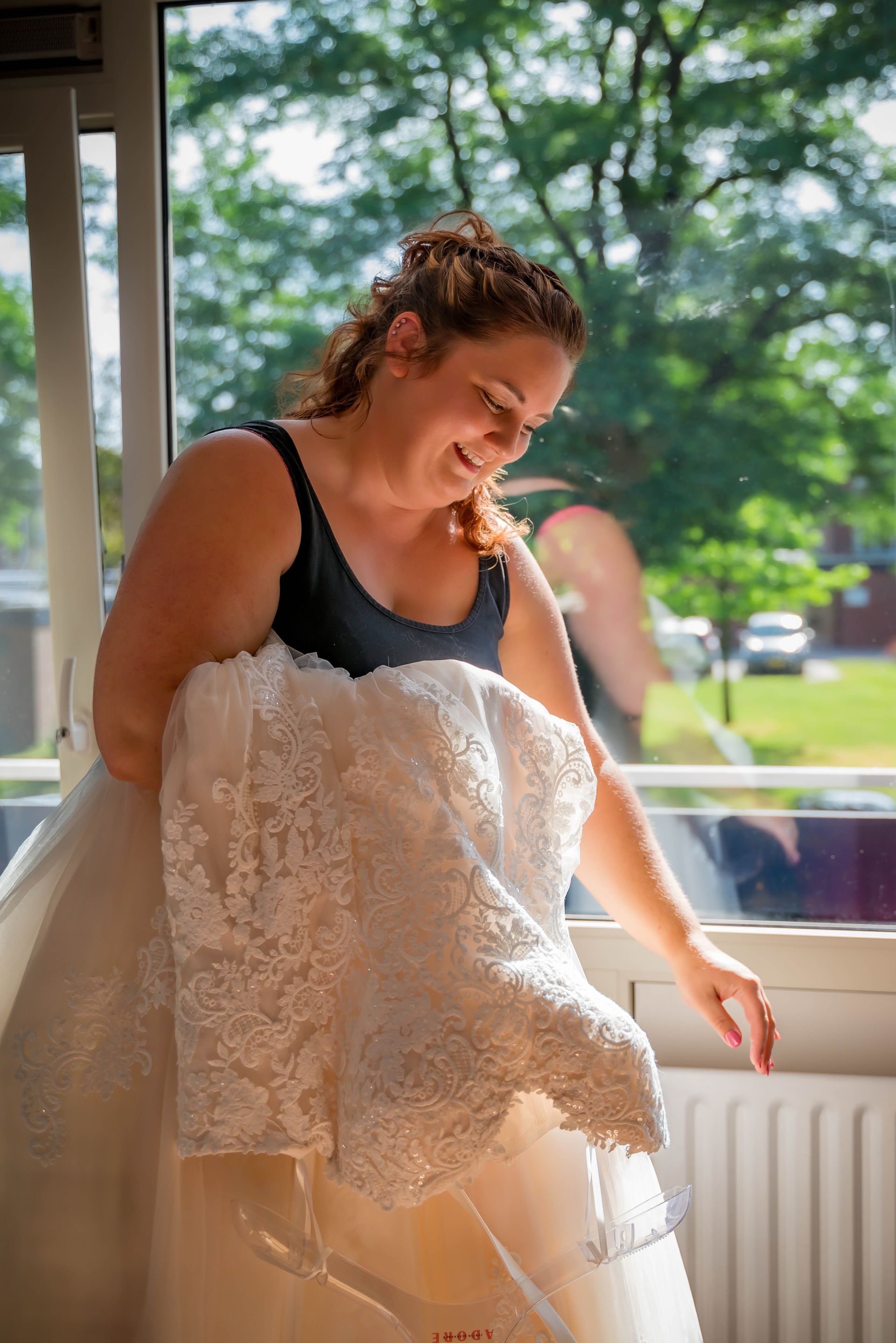 Een vrouw houdt een trouwjurk vast voor een raam.