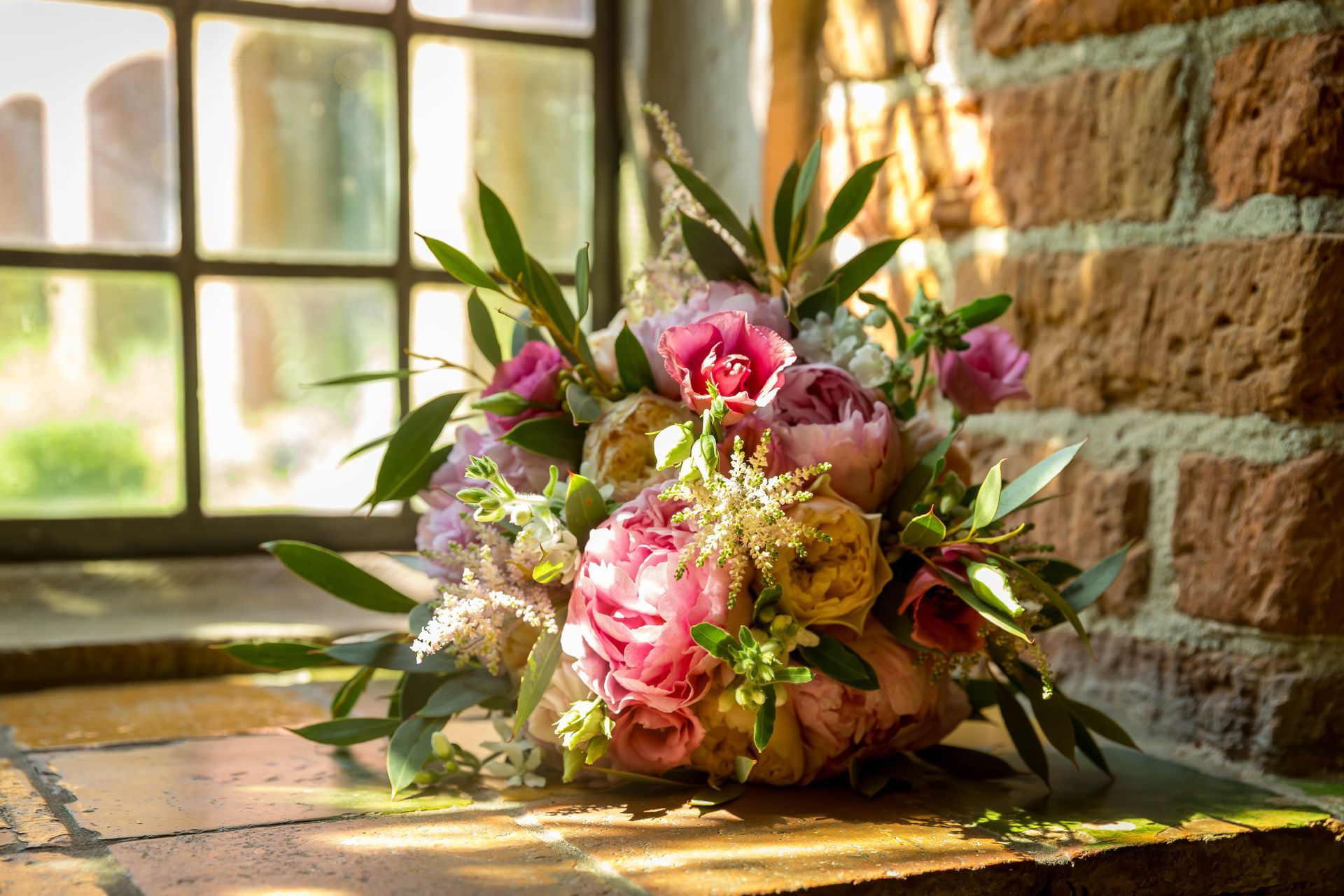 Een boeket bloemen staat op de vensterbank voor een bakstenen muur.