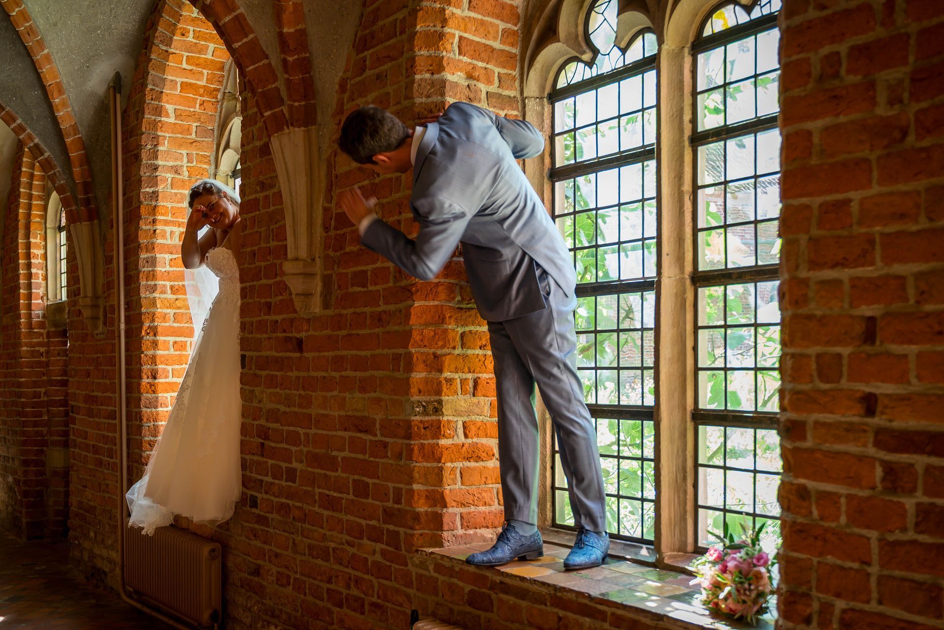 Een bruid en bruidegom poseren voor een foto voor een raam in een kerk.