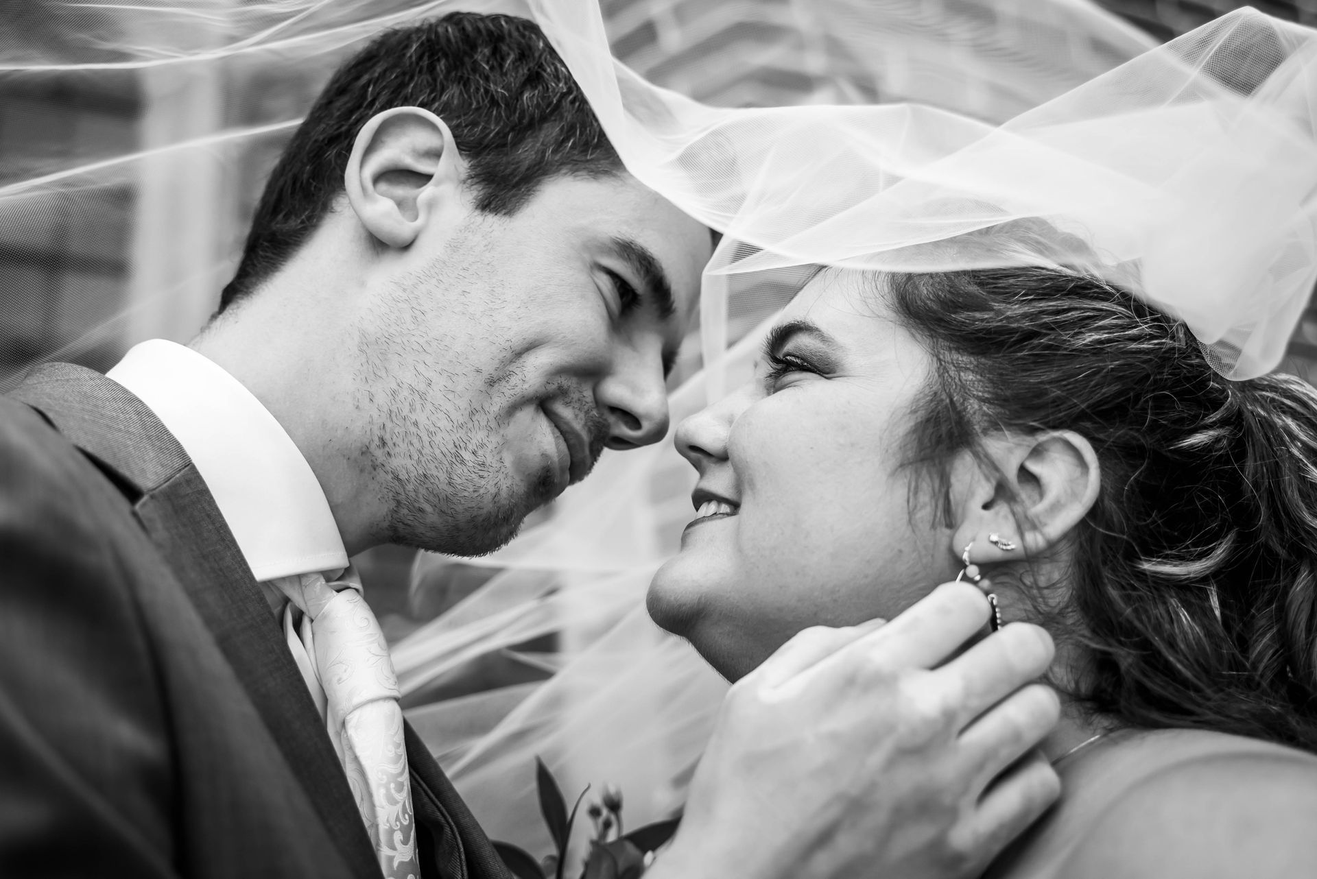 Een bruid en bruidegom kussen elkaar onder een sluier.