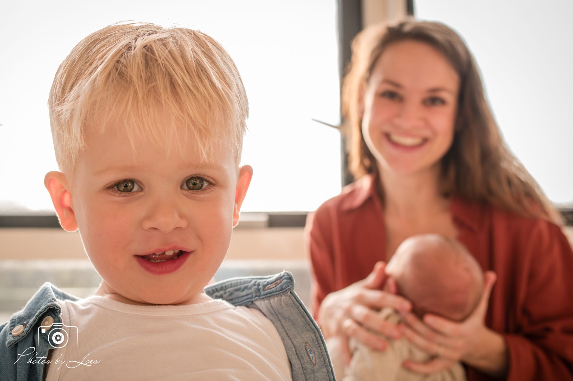 Een vrouw houdt een baby in haar armen en een jongetje staat naast haar.