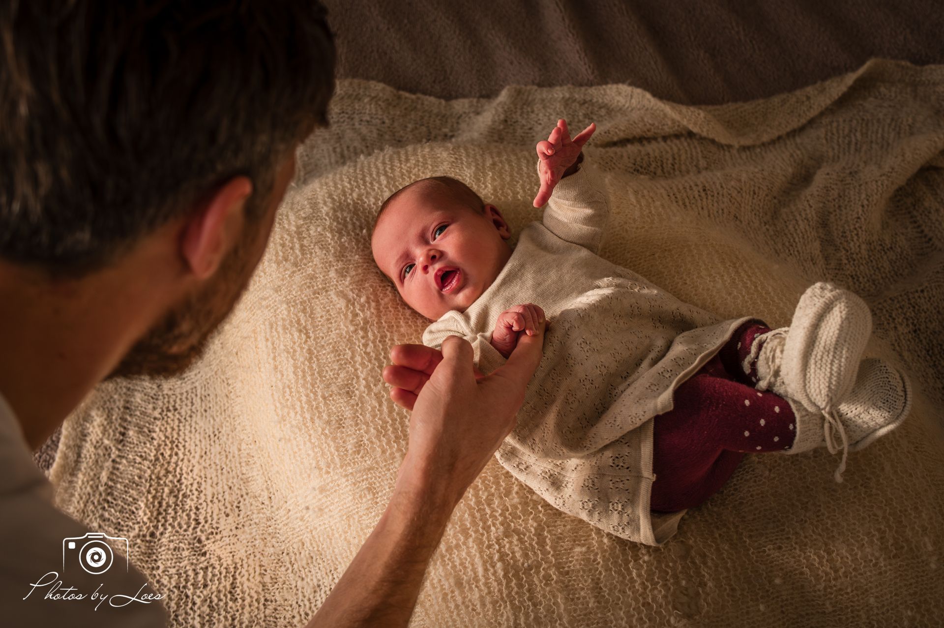 Een man houdt een baby vast op een deken op een bed.