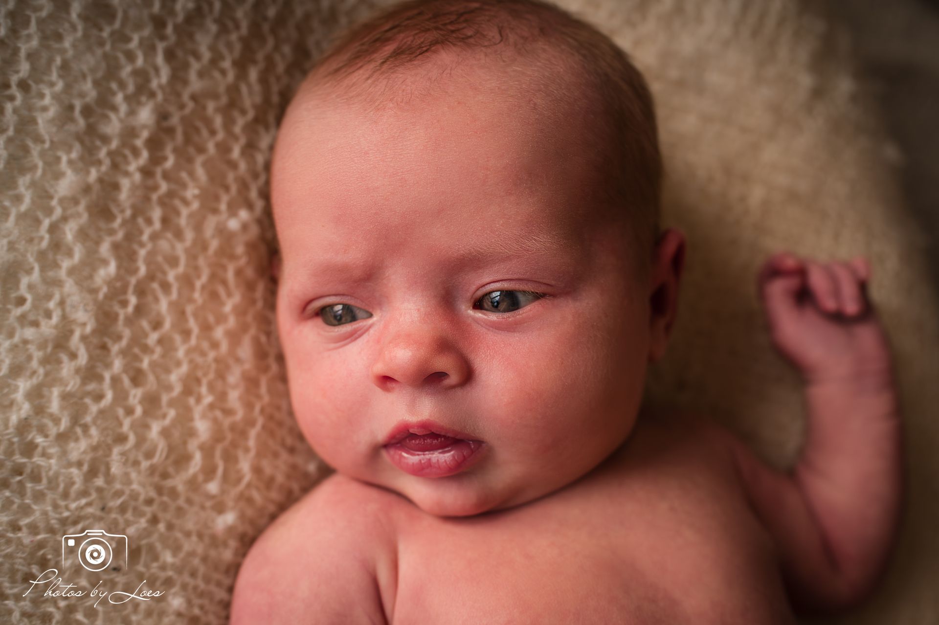 Een pasgeboren baby ligt op een deken en kijkt naar de camera.