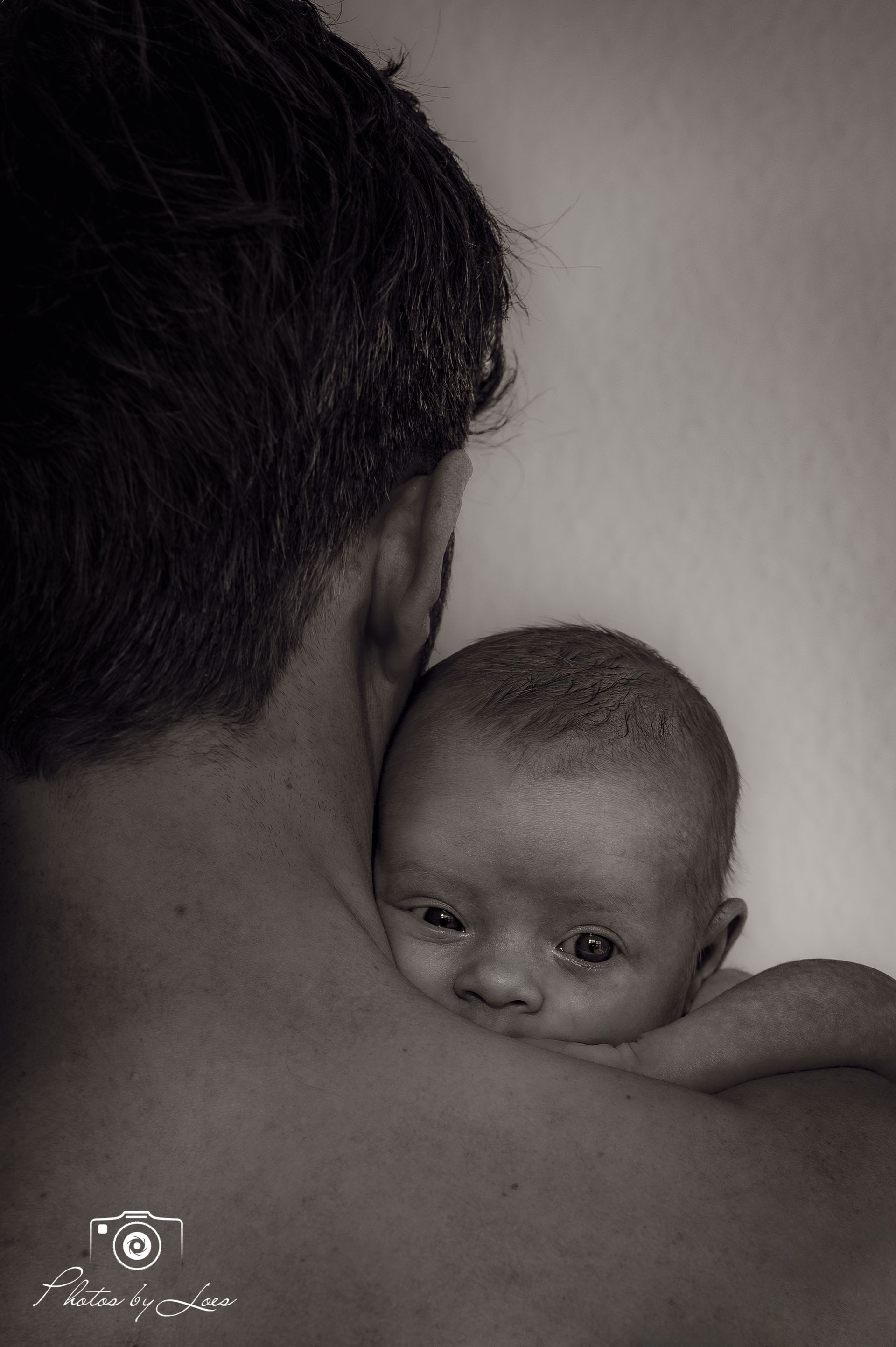 Op een zwart-witfoto houdt een man een baby op zijn schouder.