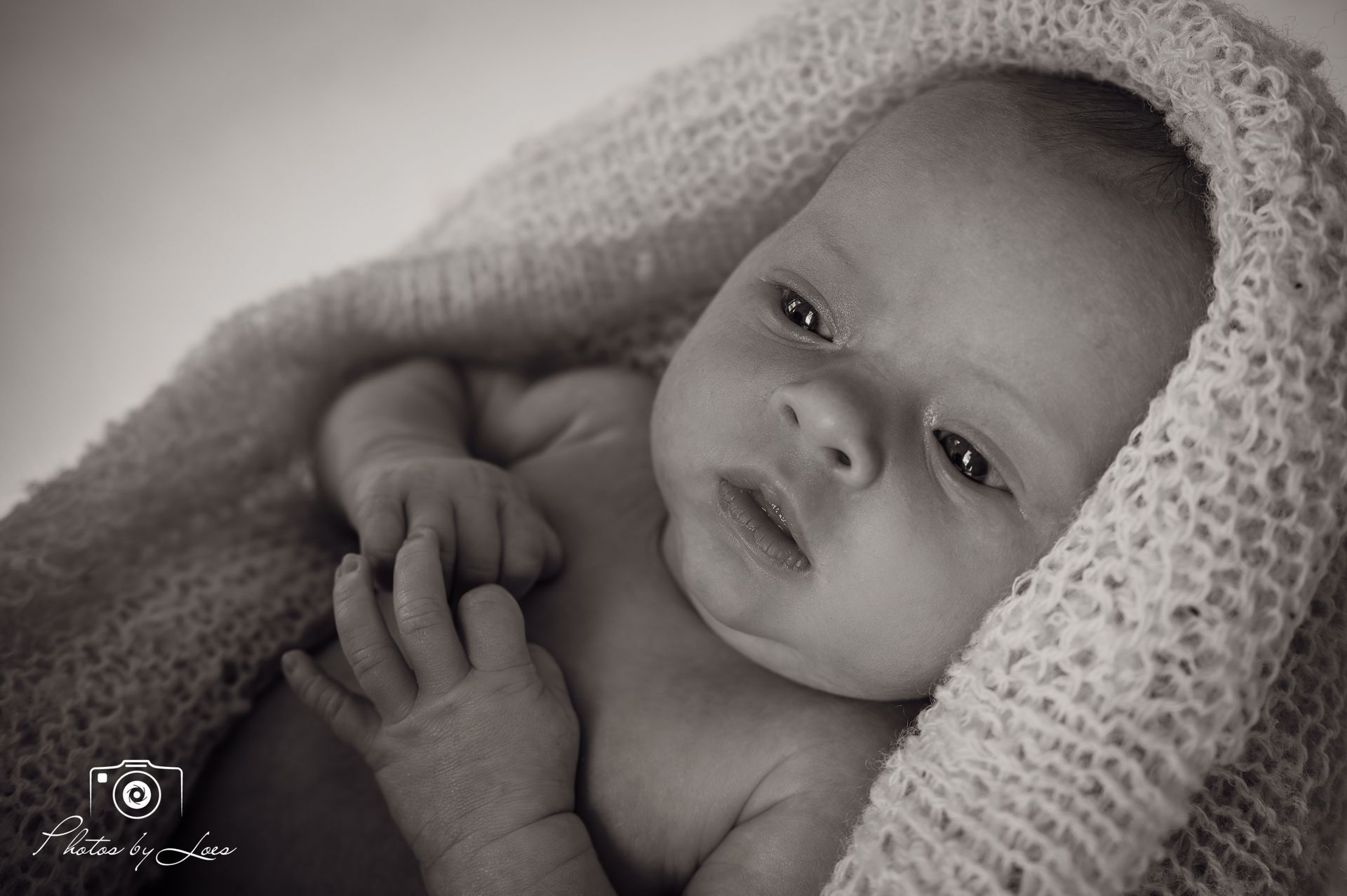 Een zwart-witfoto van een pasgeboren baby, gewikkeld in een deken.