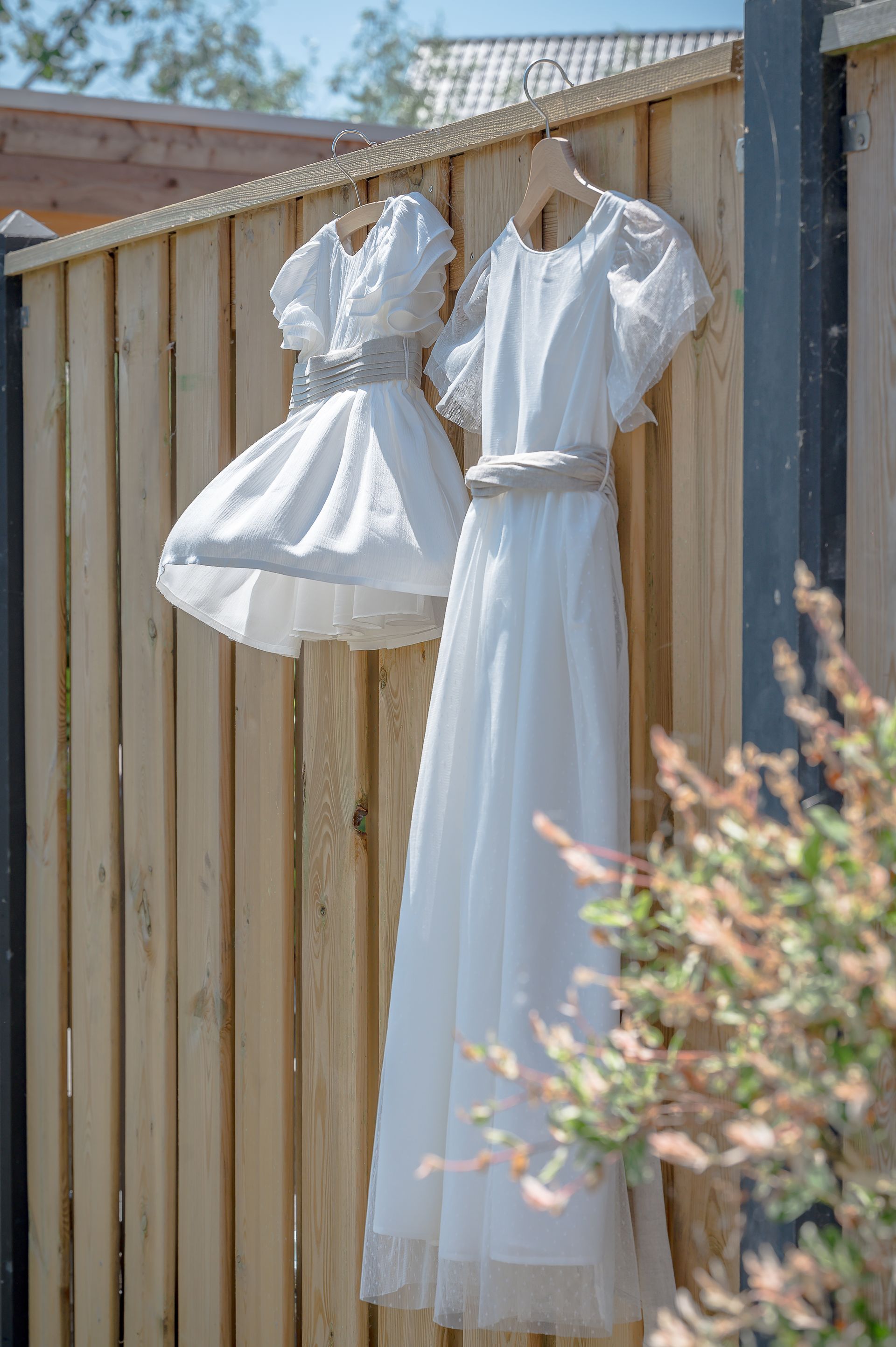 Twee witte jurken hangen aan een houten hek.