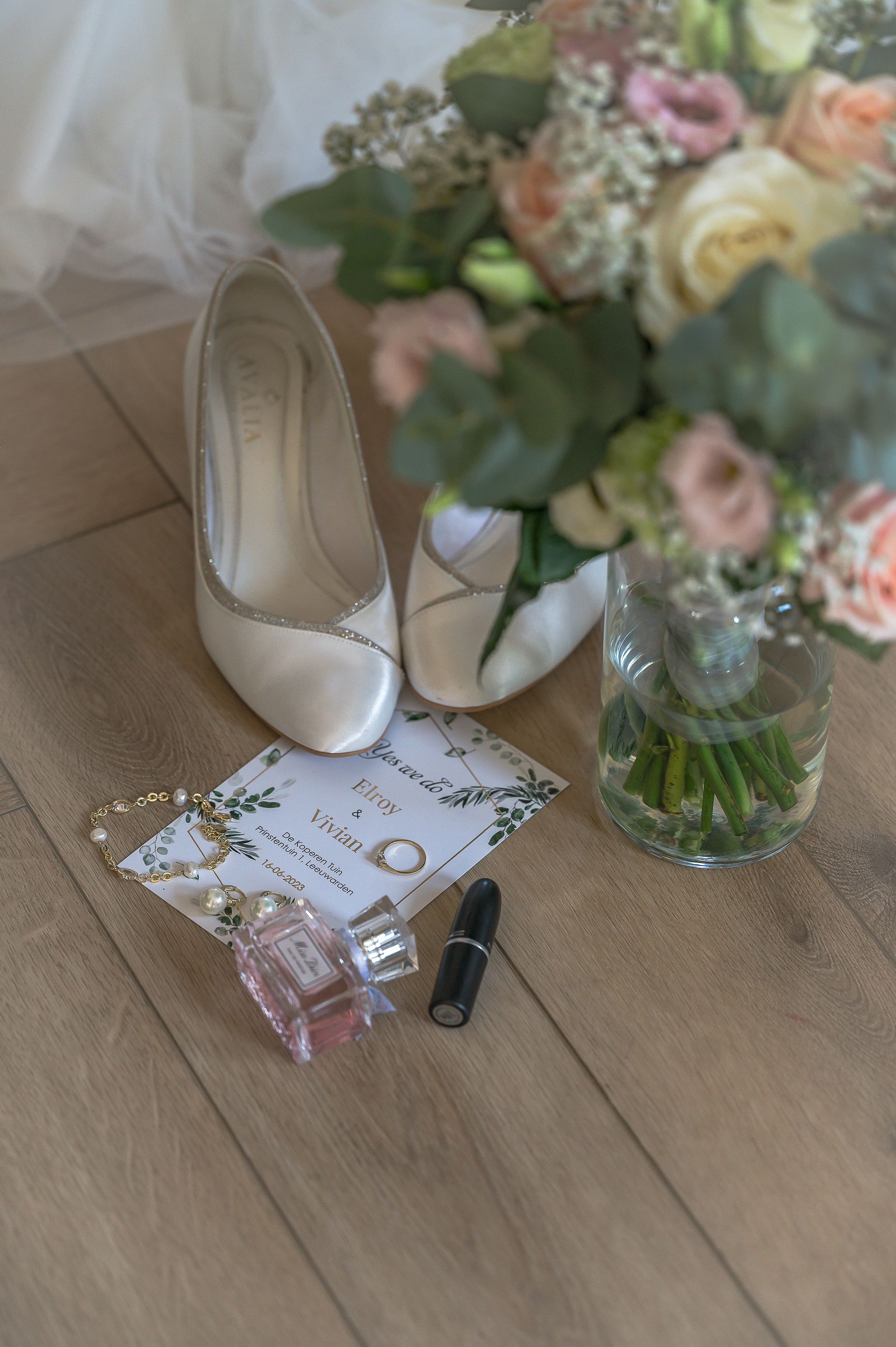 De bruidsschoenen van een bruid, sieraden en een boeket bloemen liggen op de grond.