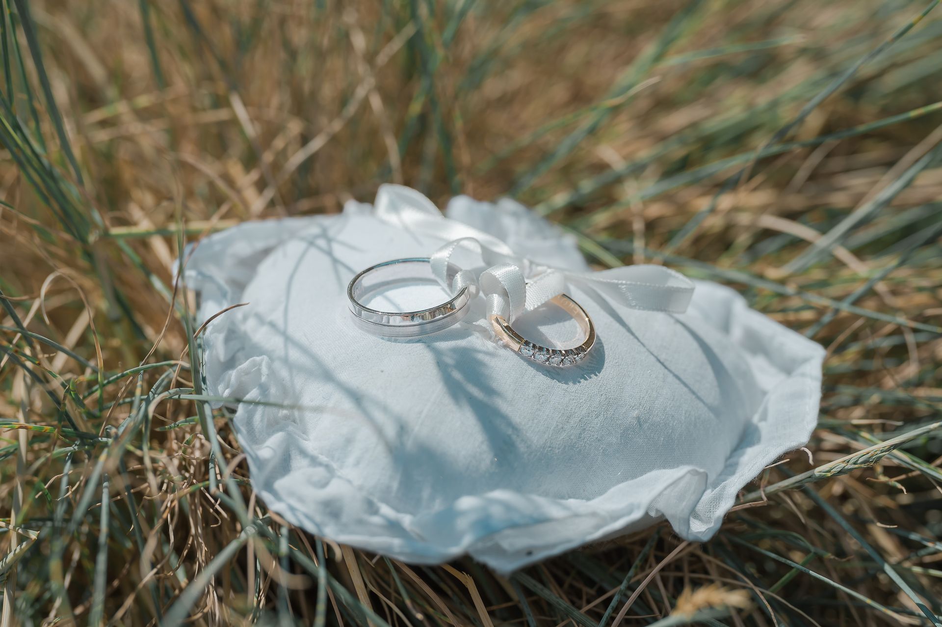 Twee trouwringen liggen op een kussen in het gras.